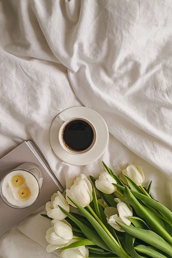 Coffee and white tulips on the bed with white bedsheets, morning still life