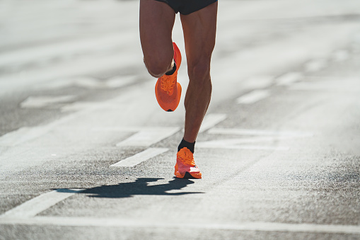 close up of male legs of one marathon runner running race on asphalt road in city