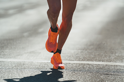 Closeup of male legs and feet in sport shoes running on asphalt road in city during marathon race