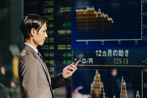 Businessmen who check the stock price charts and exchange rates on the stock price board of the electronic bulletin board and order transactions with a smartphone