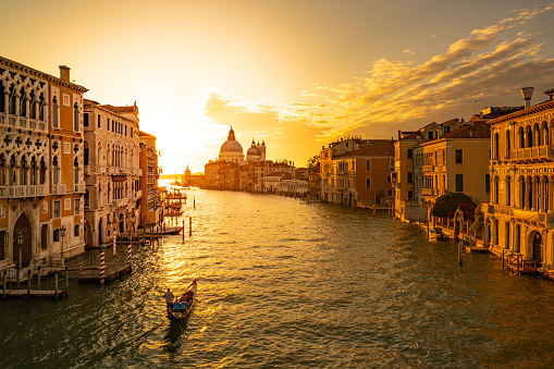 canale grande in venice italy with one gondola early in the morning and first light shining on historical buildings and houses at waterfront