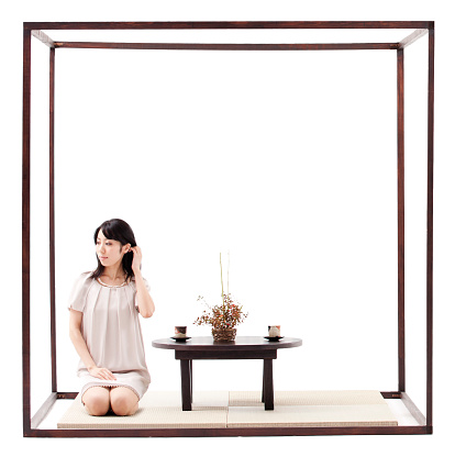 One Japanese woman, sitting within a wood framed cube, about to take tea. 