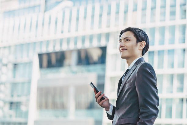 高層ビルのあるビジネス街やオフィス街で自分らしいスマートフォンを持つ30代の30代男性 - 30代 ストックフォトと画像