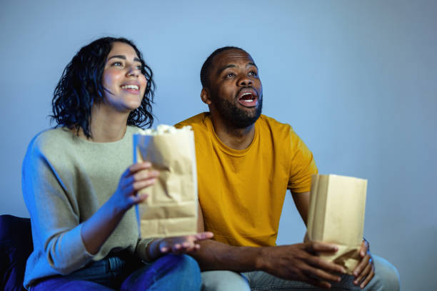 istock Young Diverse Couple Eating Popcorn and Laughing While Watching A Movie 1485019096