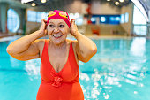 Active senior woman looking away and smiling after swim in indoors swimming pool