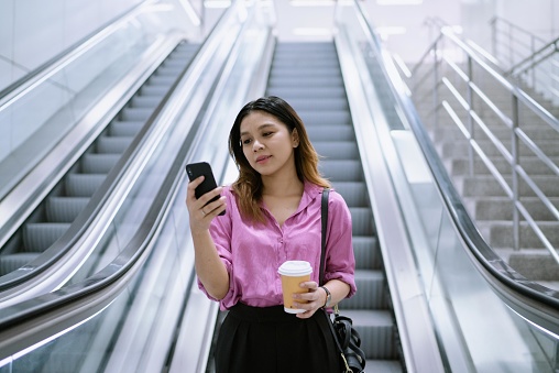 An Asian woman going down the escalator of a subway station on her way to her client's office.