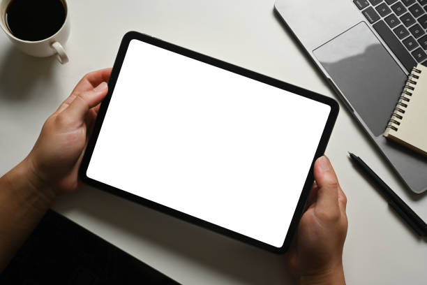 istock Man hands holding digital tablet in front of laptop at working desk. Empty screen for your advertising text message. 1485028918