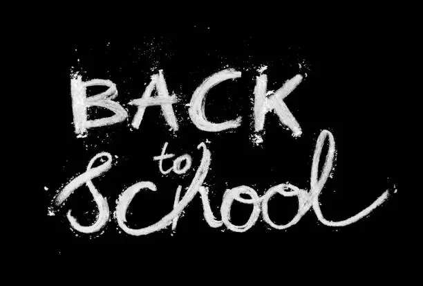 Vector illustration of BACK TO SCHOOL text scrawled on a school blackboard - messy lettering with white chalk letters with scattered crumbs around - abstract vector illustration on black background - creative design template