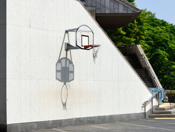 A vertical picture of a red basketball hoop on a dirty white wall during daytime