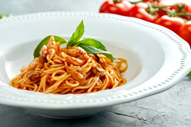 Italian spaghetti pasta with tomatoes and shrimps in a white plate on a gray background stock photo