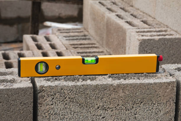 The bubble construction level lies on a cinder block construction stone. It is used to assess the compliance of surfaces with a vertical or horizontal plane, as well as to measure the angular deviatio el nivel de construcción de la burbuja se encuentra en una piedra de construcción de bloques de cemento. se utiliza para evaluar la conformidad de superficies con un plano vertical u horizontal, así como para medir la desviación angular.