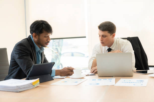 istock Two business partners actively discussing their startup projects sitting at desk, businessman and puppet chatting with colleague while looking at laptop computer and financial documents 1485037123