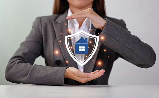 Attractive professional female hands show protecting house futuristic graphic with shield. Businesswoman sitting with white background. Property insurance and security concept