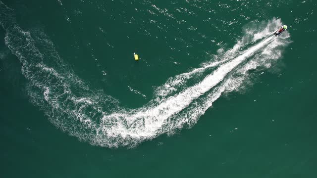 Top down aerial drone view of fast jetskier making a curve leaving a wake on the water