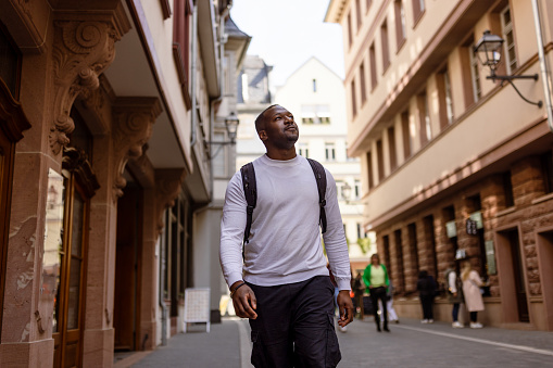 Black tourist in Frankfurt who is walking and carrying a backpack. He is dressed casually and enjoying his sightseeing experience