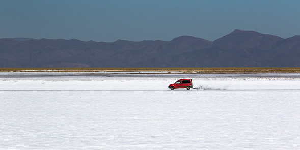Red car smoking in a white salt flat at Salinas Grandes (in the border of Salta and Jujuy Provinces, Northern Argentina). Picture was taking during a road trip, back on March 30, 2022.