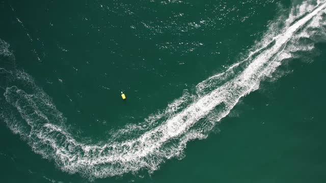 Top down aerial drone view of fast jetskier making a curve leaving a wake on the water
