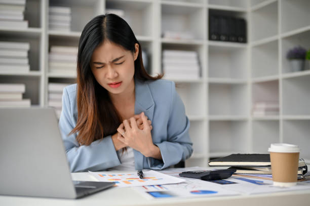 Unwell Asian businesswoman feeling chest pain, suffering from heart attack during work stock photo