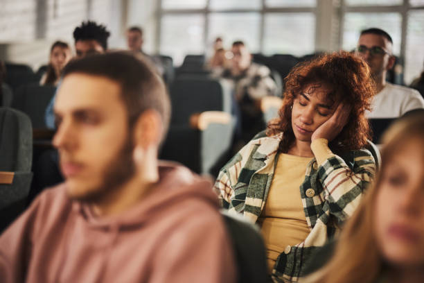 Tired black female student taking a nap on a class in amphitheater. Exhausted African American female student taking a nap on a class at lecture hall. male college student sleeping through lecture stock pictures, royalty-free photos & images