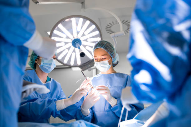 team of professional doctors performing operation in surgery room. medical team performing surgical operation in bright modern operating room - operação imagens e fotografias de stock