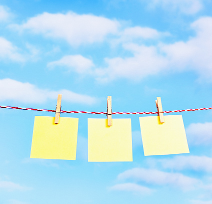 Clothespins fasten three blank yellow notes to a washline in bright sunshine, all ready for your message.