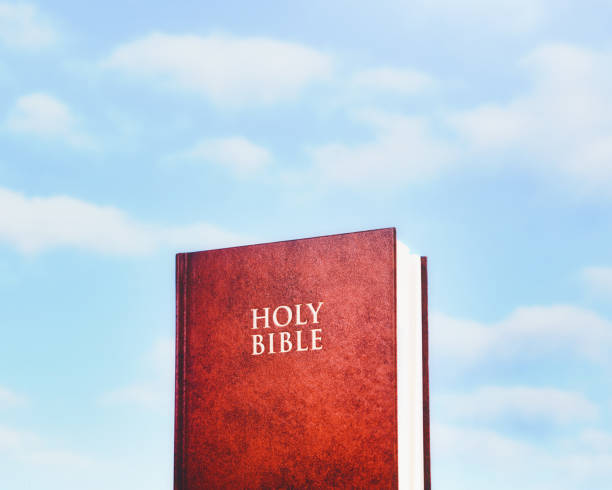 A closed copy of the Holy Bible stands against a heavenly background.