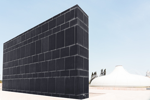 Jerusalem, Israel - April 25, 2019: Jerusalem modern Black Basalt Wall which symbolizes the Sons of Darkness close to the white Dome of the Shrine of the Book under blue clear summer sky. Jerusalem, Israel, Middle East.