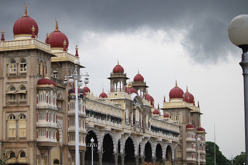 The ornate Mysore Palace building with red dome-shaped roofs on the background of cloudy sky