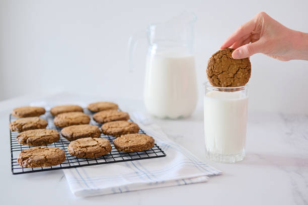 mano della donna che immerge i biscotti fatti in casa in un bicchiere di latte - biscotti cookie morning temptation foto e immagini stock