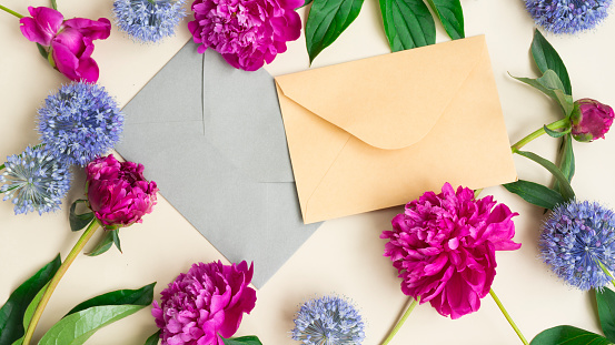 Flay lay of an envelope in between scattered lisianthus flowers and a pink book against a pastel pink background.