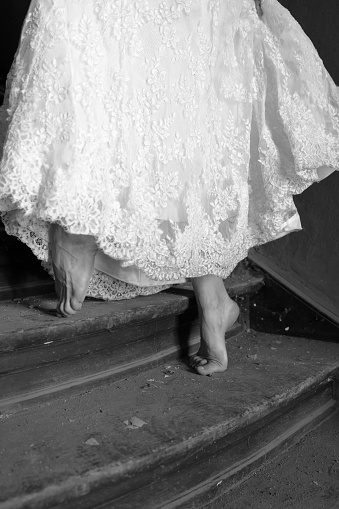 Old and dirty wooden stairs with detail of a woman,s legs wearing a wedding dress.