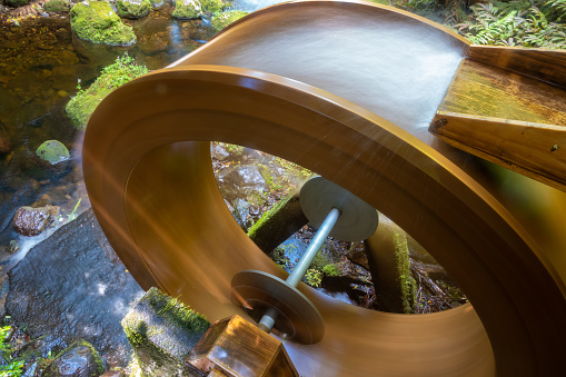 A wooden water wheel turns water along the River Aure at an old stone mill in Bayeux, France, in the Normandy region during autumn with fall colors on the leaves. Bayeux is a town on the Aure river in the Normandy region of northwestern France, 10 kilometers from the Channel coast. Its medieval center contains cobbled streets, half-timbered houses and the towering, Norman-Gothic Cathédrale Notre-Dame.