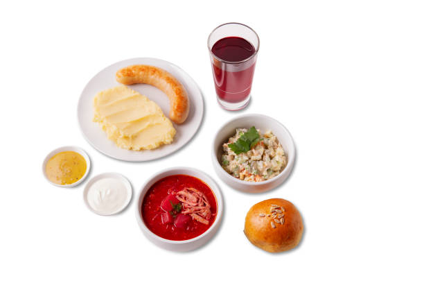 Complex lunch. Mashed potatoes with sausage in a plate with sauces in bowls, borscht, olivier salad, bun with seeds and compote in a glass standing on a white background