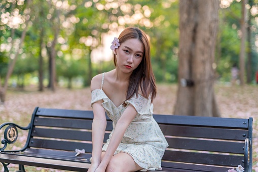 Portrait photo of young asian woman enjoying her relax time in a lush greenery park during sunset moment. Half body shot. Beautiful asian woman