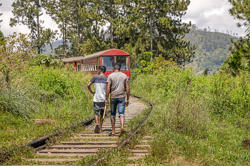 Nine Arch Bridge, Ella, Uva Province, Sri Lanka - February 18th 2023:  Two men walking on the trail behind a passing train. The trails are often used as paths for pedestrians in Sri Lanka