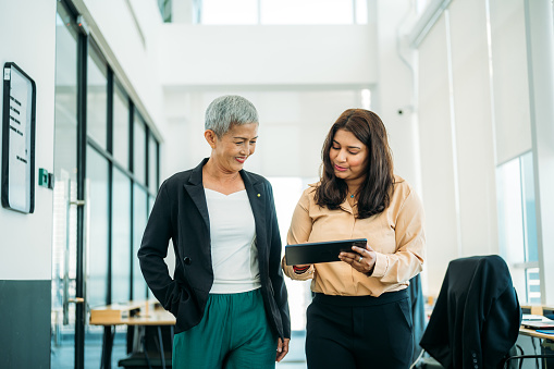 Two multiethnic female business partners are working together, discussing ideas at a modern office. Corporate business persons discussing new project and sharing ideas in the workplace.