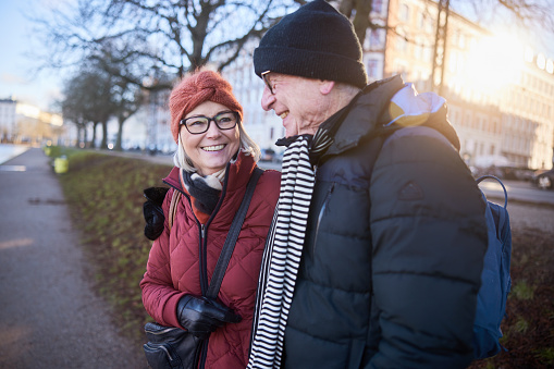 Senior couple smiling while standing arm in arm awhile out for a walk together in a city park in winter