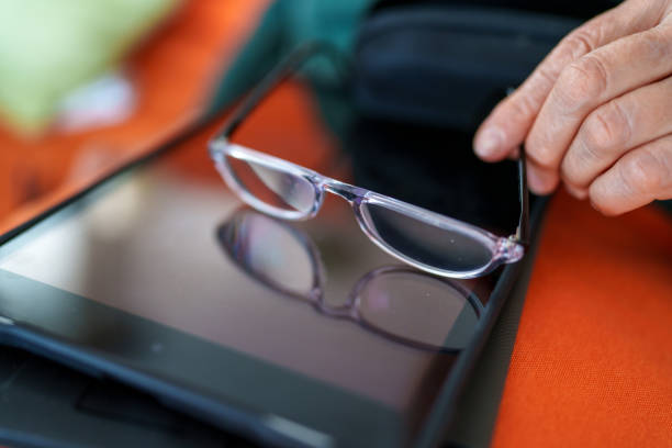 The elderly woman is cleaning her reading glasses to use her digital tablet.