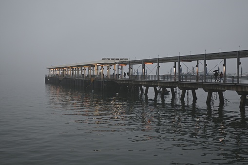 A beautiful view of a pier over the lake on a cold foggy day