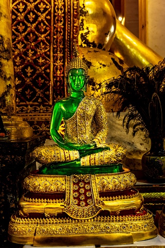 A vibrant green Buddha statue sits in a tranquil temple setting, with a peaceful ambiance