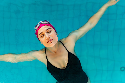 Woman floating on her back in the indoor swimming pool during the day.