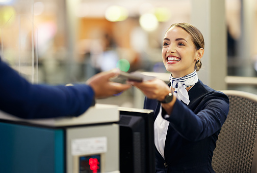 Woman, airport and passenger assistant with passport helping traveler for check in at terminal counter. Female service agent with smile in travel security or immigration documents for airline control