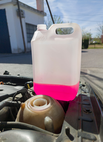 Bottle of antifreeze close to liquid tank. Old diesel engine background