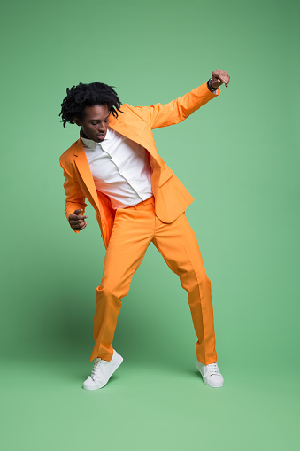 Fashion portrait of elegant man wearing orange suit and white shirt dancing against green background. Studio shot.