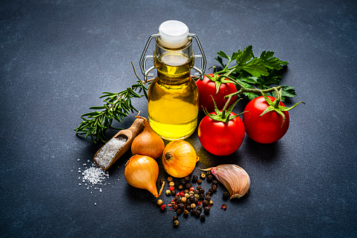 Close up view of vegetarian ingredients for healthy cooking on dark background. The composition includes extra virgin olive oil bottle, ripe tomatoes, parsley, rosemary, onion, garlic salt and peppercorns. High resolution 42Mp studio digital capture taken with SONY A7rII and Zeiss Batis 40mm F2.0 CF lens