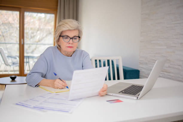 istock Senior woman using calculator while going through bills and home finances 1485099573