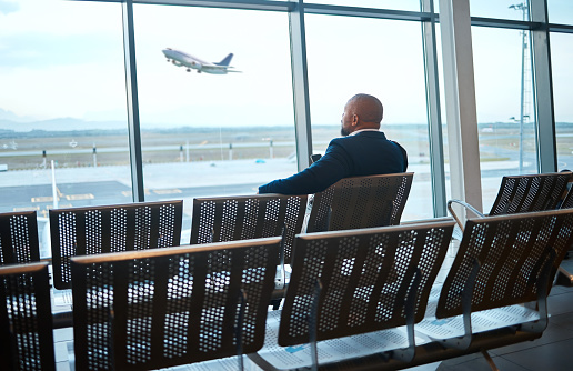 Airport waiting, black man back and phone for work travel, plane and air flight. Businessman, mobile connection and person sitting with cellphone looking at traveler app info for airplane traveling