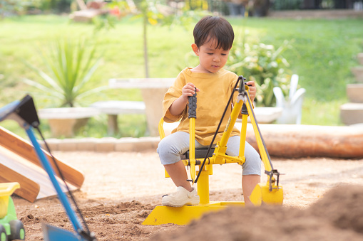 Kid Asian baby boy todler playing construction truck toy digging sand in playground
