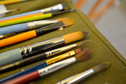 artist's palette with oil paints Close up of a series of used brushes in an artist's studio. Paint brushes in a row, Palette at background natural light