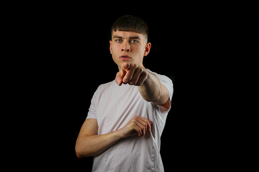 A portrait of a teenage boy with a serious expression and pointing against a black background